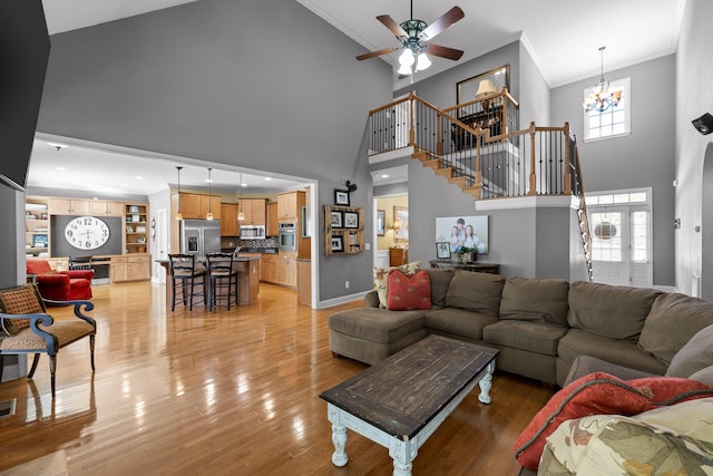 living room featuring a high ceiling, ornamental molding, ceiling fan with notable chandelier, and light hardwood / wood-style flooring