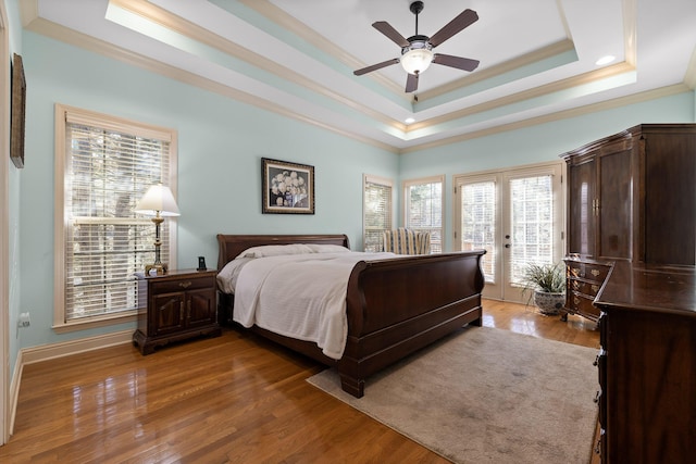 bedroom featuring wood-type flooring, access to exterior, a tray ceiling, crown molding, and french doors