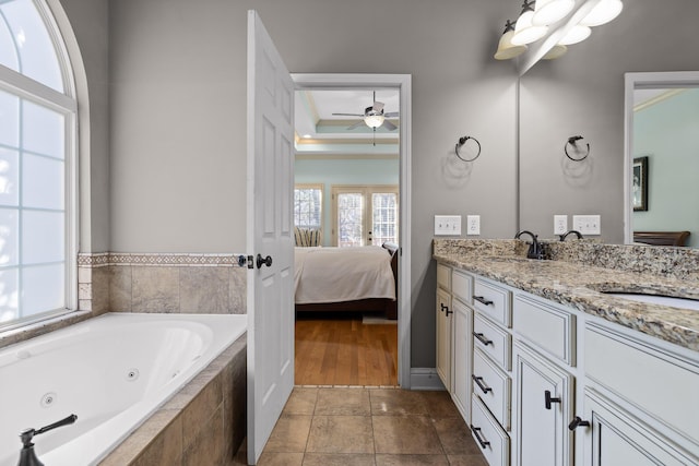 bathroom with tiled tub, ceiling fan, vanity, french doors, and a raised ceiling