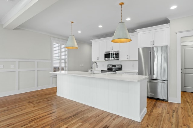 kitchen with pendant lighting, sink, white cabinetry, stainless steel appliances, and a center island with sink