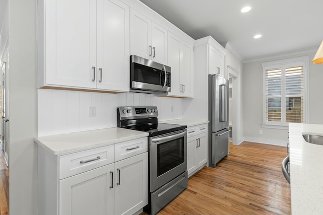 kitchen with white cabinets, light stone counters, light hardwood / wood-style floors, stainless steel appliances, and crown molding