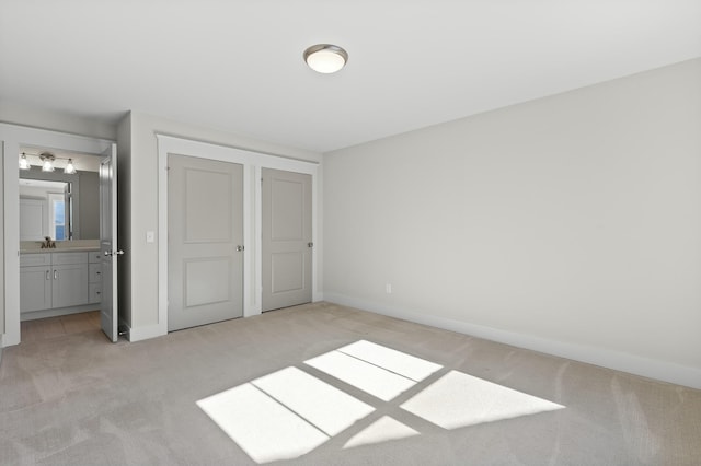 unfurnished bedroom featuring baseboards, ensuite bathroom, a sink, and light colored carpet