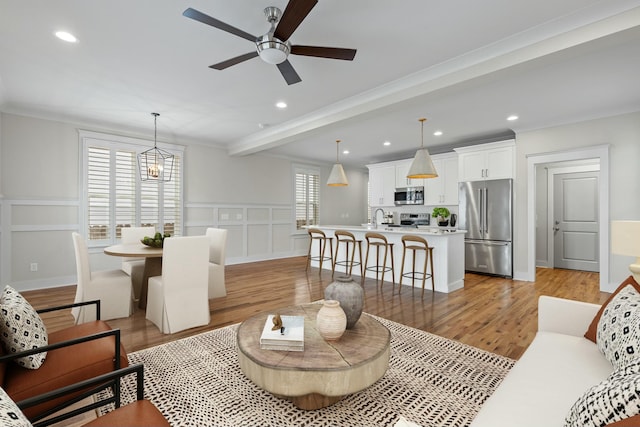 living room with sink, ornamental molding, ceiling fan, light hardwood / wood-style floors, and beam ceiling