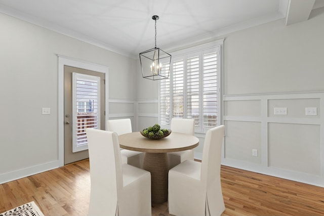 dining space with light wood-type flooring, a notable chandelier, a decorative wall, and crown molding