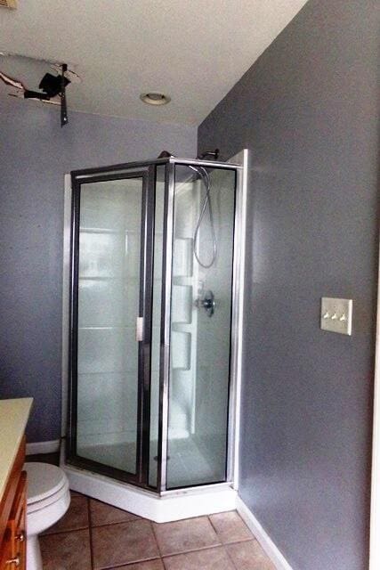 bathroom featuring tile patterned flooring, vanity, toilet, and walk in shower