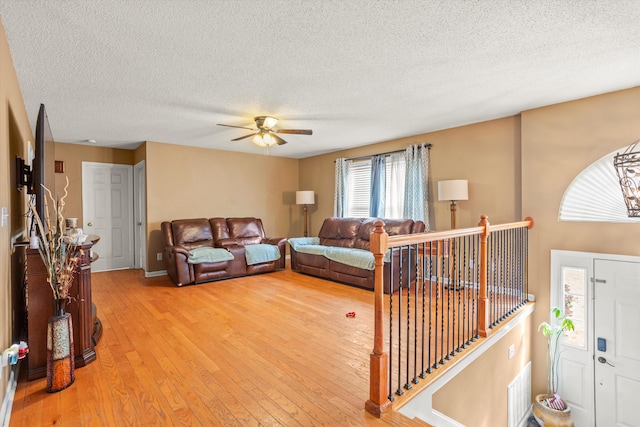 living room with ceiling fan, light hardwood / wood-style flooring, and a textured ceiling