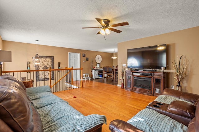 living room with ceiling fan with notable chandelier, hardwood / wood-style floors, and a textured ceiling