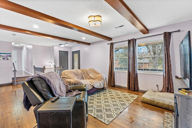 living room featuring light wood-type flooring, a textured ceiling, and beam ceiling