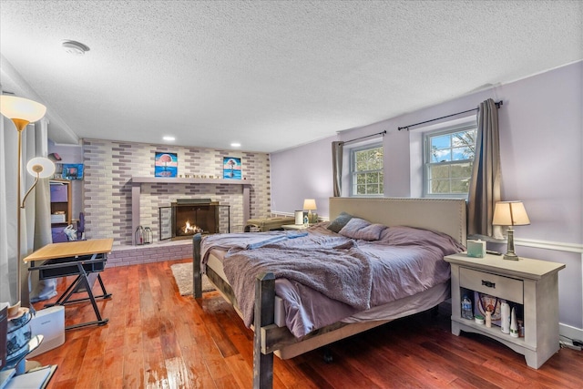 bedroom featuring a brick fireplace, hardwood / wood-style flooring, and a textured ceiling