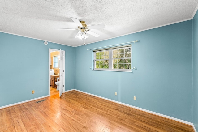 unfurnished bedroom featuring ceiling fan, ensuite bathroom, ornamental molding, a textured ceiling, and light wood-type flooring