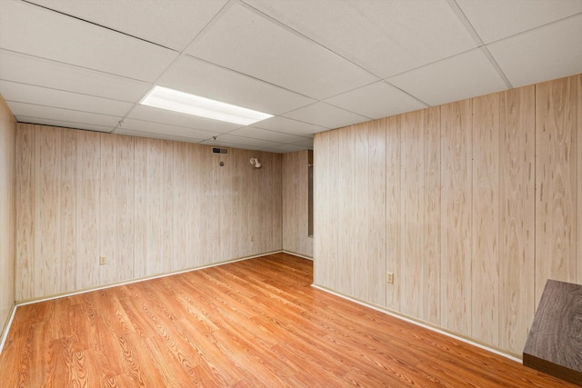 unfurnished room with a drop ceiling, wooden walls, and light wood-type flooring