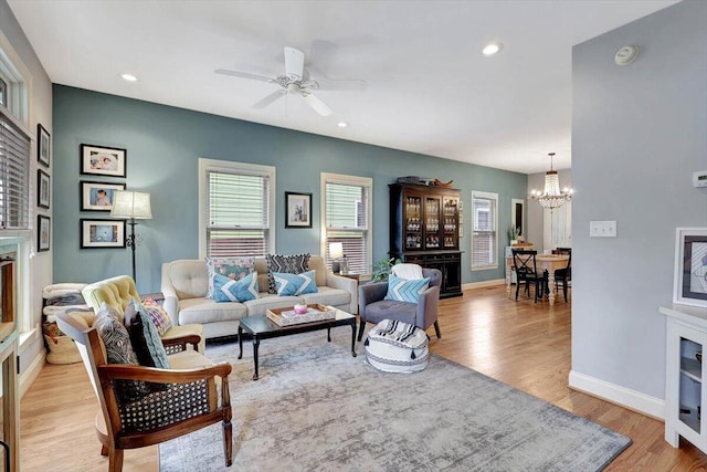 living room with ceiling fan with notable chandelier, a fireplace, and light hardwood / wood-style floors