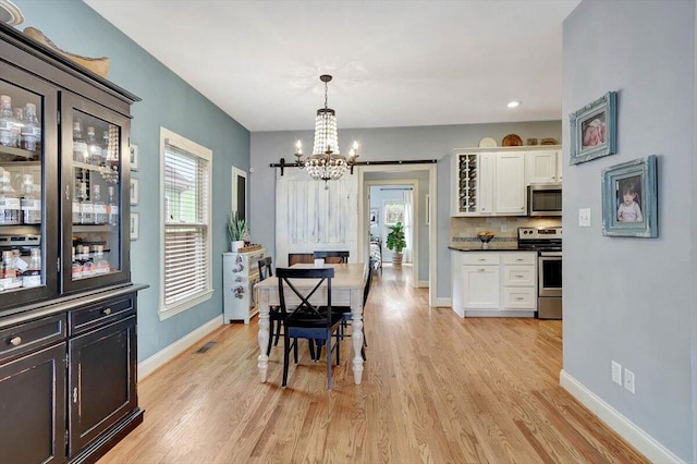 dining space featuring a barn door, a chandelier, and light wood-type flooring