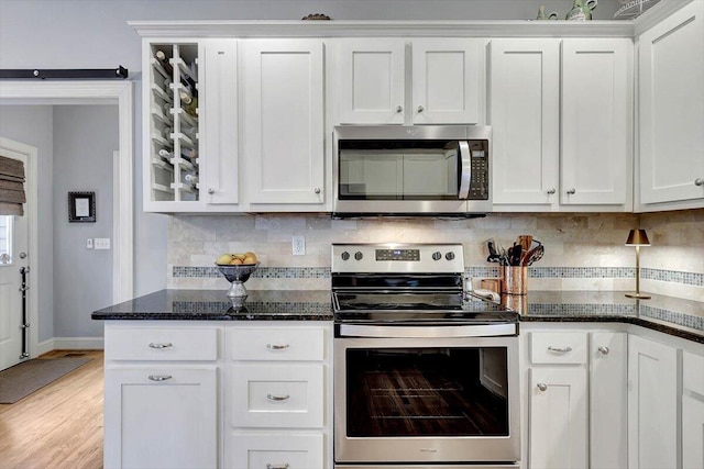 kitchen with decorative backsplash, dark stone counters, white cabinets, and appliances with stainless steel finishes