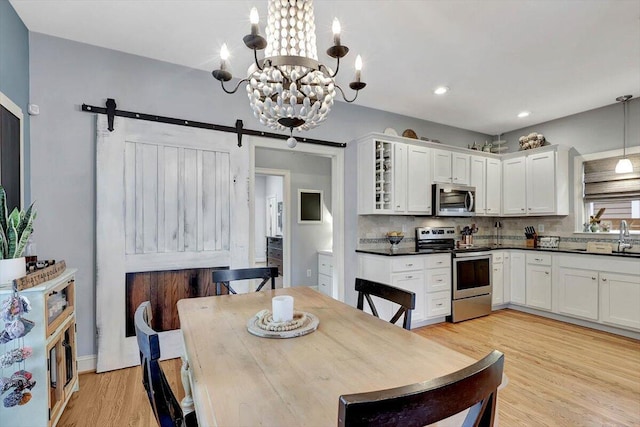 dining area with a barn door, an inviting chandelier, and light wood-type flooring