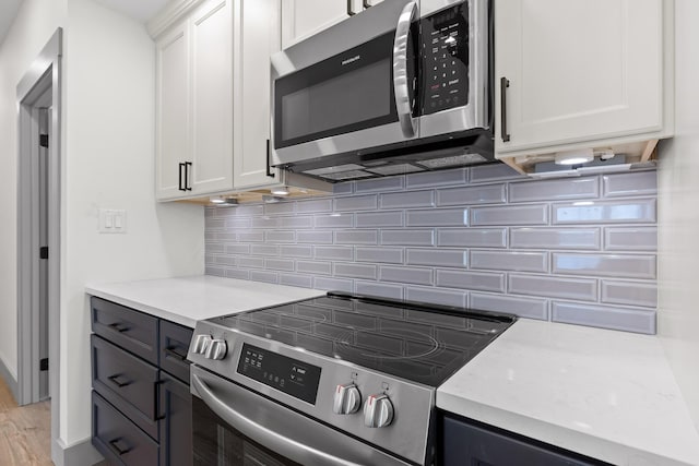 kitchen with white cabinets, decorative backsplash, appliances with stainless steel finishes, light stone counters, and light wood-style floors