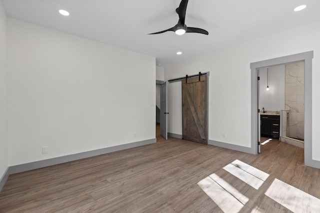 unfurnished bedroom with recessed lighting, wood finished floors, baseboards, and a barn door