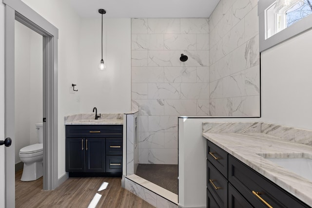 bathroom with a sink, a walk in shower, two vanities, and wood finished floors