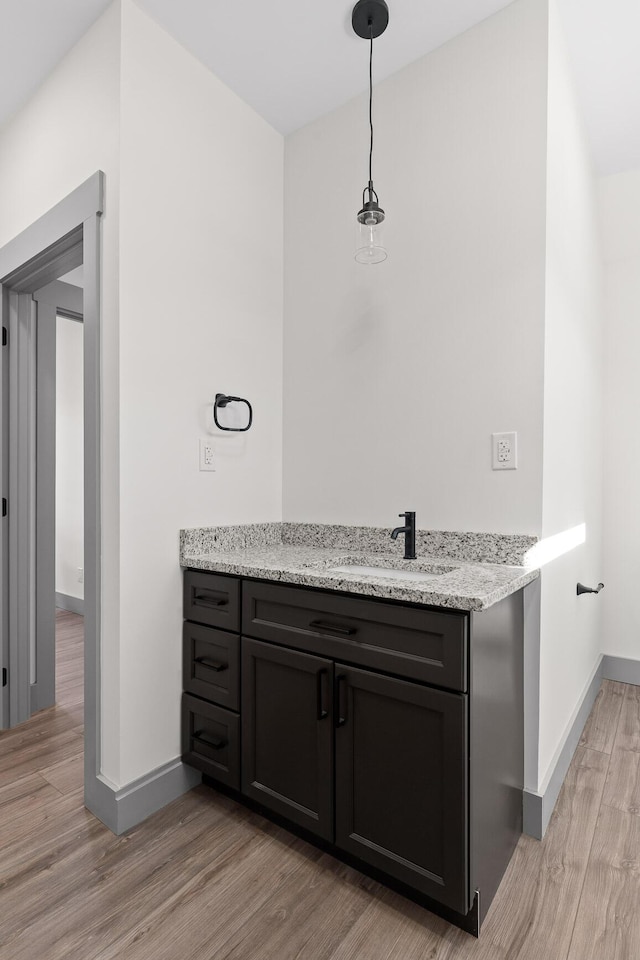 interior space featuring hanging light fixtures, light wood finished floors, a sink, and baseboards