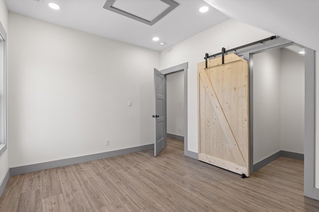 unfurnished bedroom with recessed lighting, wood finished floors, baseboards, and a barn door