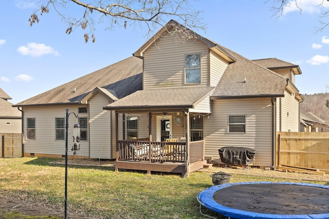 back of house with a deck, a fire pit, a trampoline, and a lawn