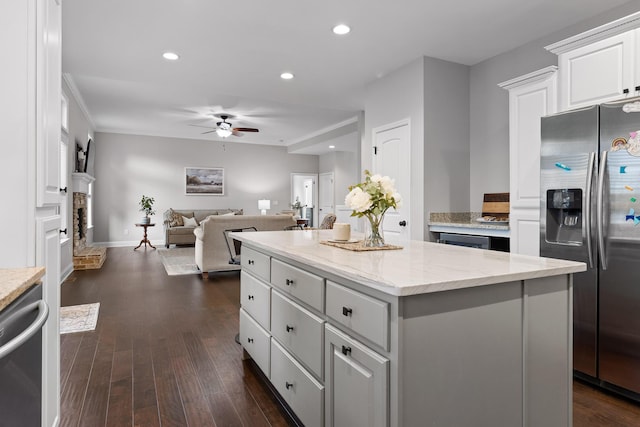 kitchen with dark wood-type flooring, stainless steel appliances, light stone countertops, white cabinets, and a kitchen island