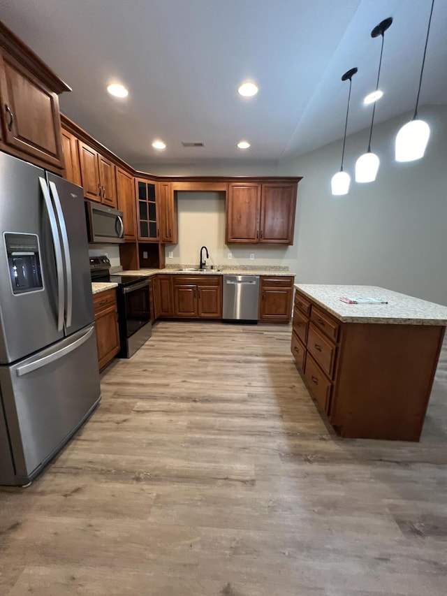 kitchen with appliances with stainless steel finishes, sink, hanging light fixtures, light hardwood / wood-style floors, and light stone countertops