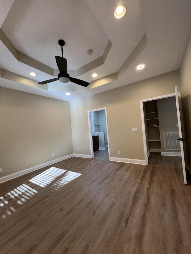 unfurnished bedroom with ensuite bathroom, a spacious closet, dark hardwood / wood-style flooring, and a tray ceiling