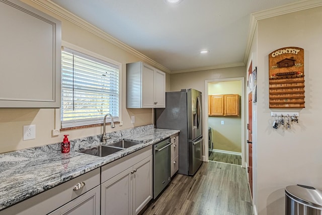 kitchen with appliances with stainless steel finishes, hardwood / wood-style floors, sink, ornamental molding, and light stone counters