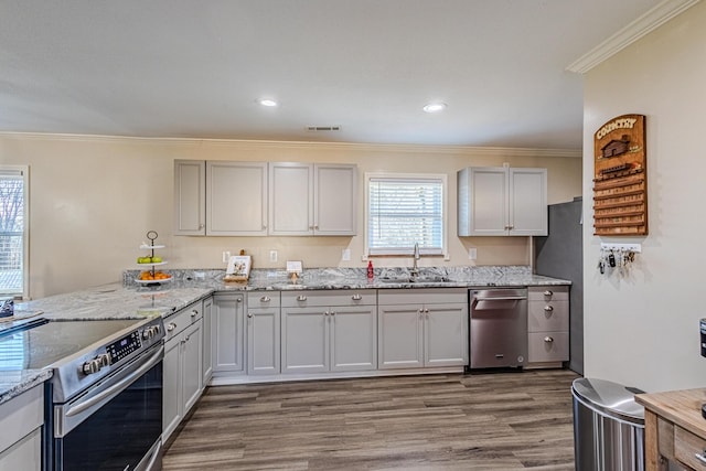 kitchen featuring sink, hardwood / wood-style floors, stainless steel appliances, light stone counters, and ornamental molding