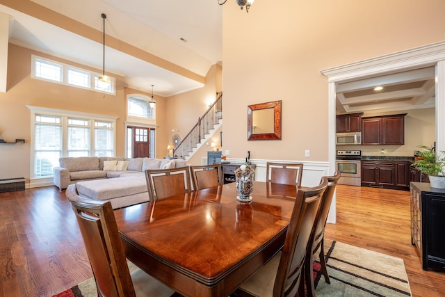 dining room with crown molding, a high ceiling, coffered ceiling, light hardwood / wood-style floors, and beamed ceiling