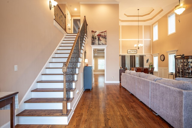 stairway featuring hardwood / wood-style flooring, ornamental molding, a chandelier, and a high ceiling