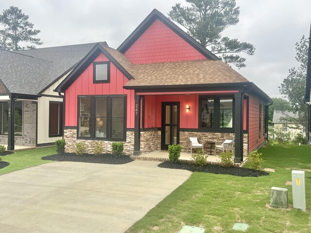 craftsman house featuring a shingled roof, board and batten siding, a porch, a front lawn, and stone siding