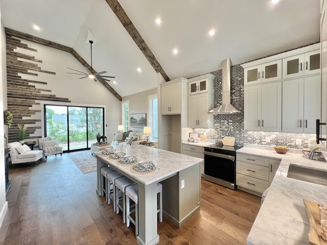 kitchen with stainless steel electric range, wall chimney exhaust hood, open floor plan, a ceiling fan, and high vaulted ceiling