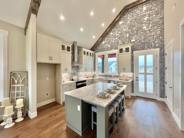 kitchen with wall chimney exhaust hood, a kitchen island, wood finished floors, backsplash, and high vaulted ceiling