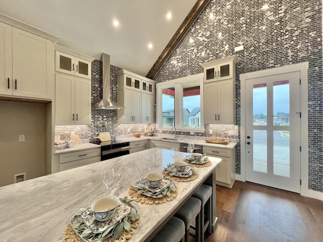 kitchen with wall chimney exhaust hood, plenty of natural light, a breakfast bar area, range with electric cooktop, and high vaulted ceiling