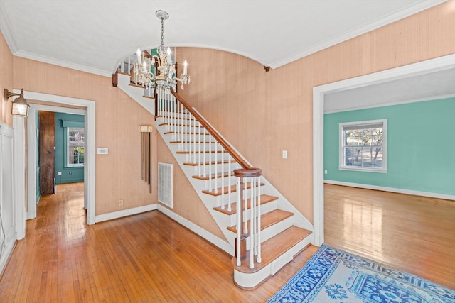 stairs with hardwood / wood-style floors, crown molding, and a notable chandelier