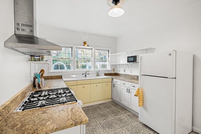 kitchen featuring sink, white cabinetry, white fridge, stainless steel gas stovetop, and wall chimney range hood