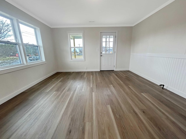 entryway featuring a wainscoted wall, baseboards, crown molding, and wood finished floors