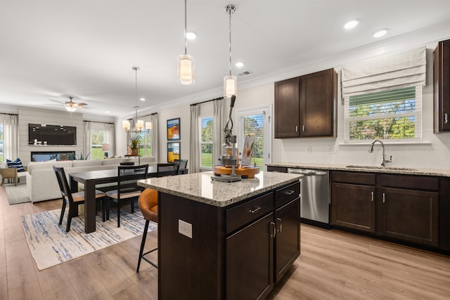 kitchen with sink, light stone counters, a kitchen island, decorative light fixtures, and stainless steel dishwasher