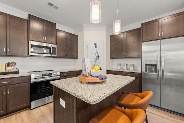 kitchen featuring a kitchen island, appliances with stainless steel finishes, dark brown cabinets, and a breakfast bar