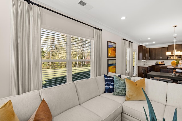 living room featuring sink, crown molding, a wealth of natural light, and a notable chandelier