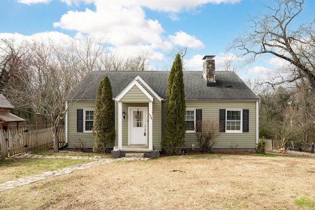 new england style home with a shingled roof, a front yard, fence, and a chimney