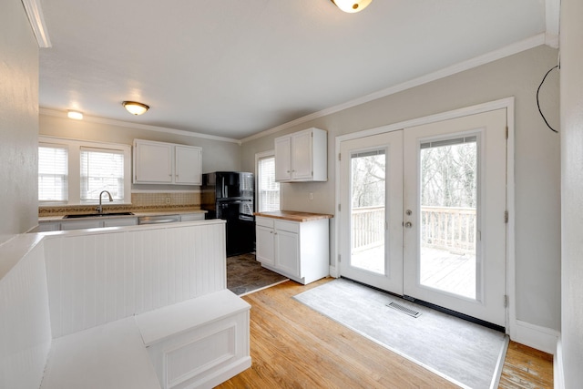 kitchen featuring white cabinetry, ornamental molding, light hardwood / wood-style floors, and black fridge