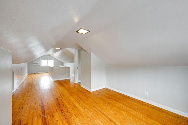 additional living space featuring hardwood / wood-style flooring, a wall unit AC, and lofted ceiling