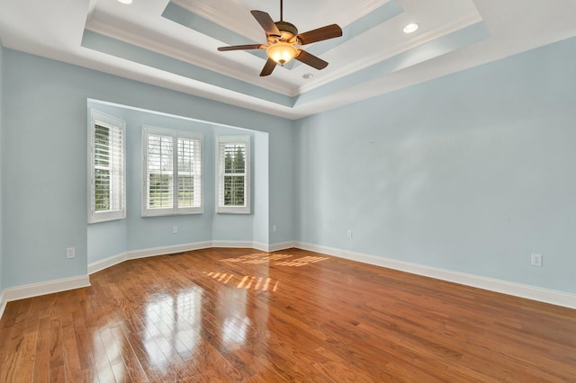 unfurnished room featuring a ceiling fan, baseboards, a tray ceiling, wood-type flooring, and crown molding