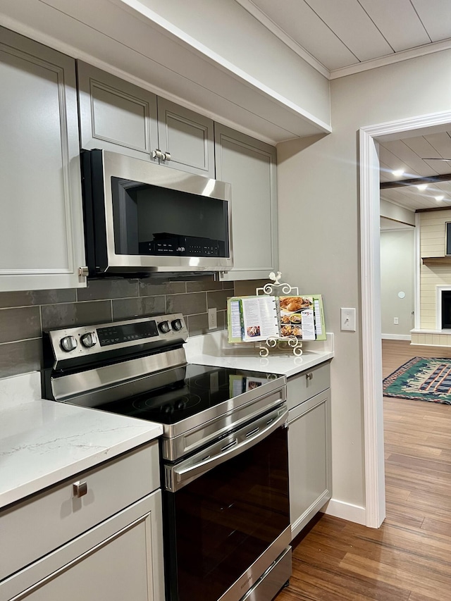 kitchen with dark wood-style floors, appliances with stainless steel finishes, gray cabinets, crown molding, and backsplash