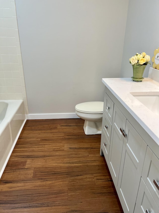 full bath with toilet, a washtub, wood finished floors, vanity, and baseboards