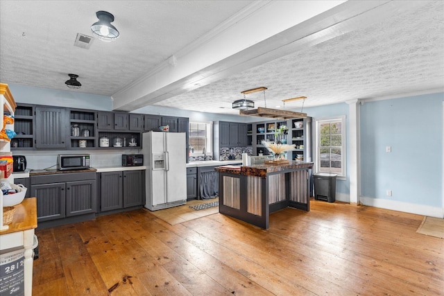 kitchen featuring decorative light fixtures, white refrigerator with ice dispenser, a center island, a textured ceiling, and light hardwood / wood-style flooring