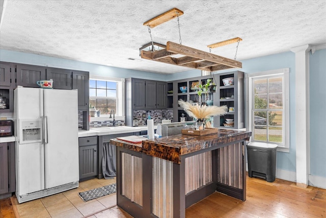 kitchen featuring a kitchen island, decorative light fixtures, tasteful backsplash, sink, and white refrigerator with ice dispenser